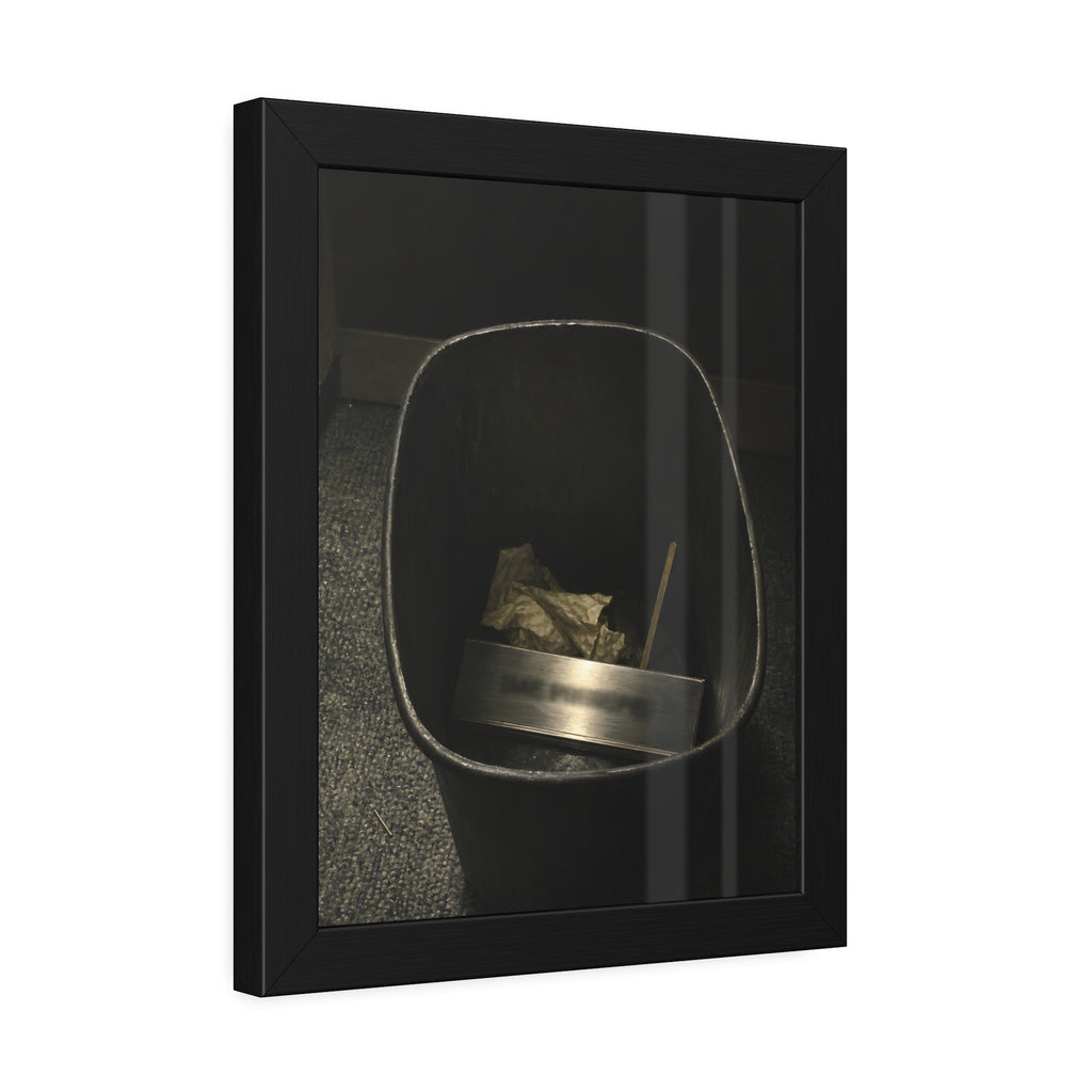 A metal nameplate lying in a black office waste bin on grey carpet. The Nameplate in the Waste Bin by Garabaggio, framed fine art print hanging in a room.