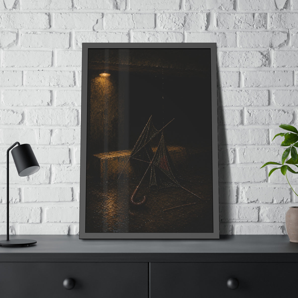 A broken umbrella collapsed on wet ground below a loading dock lamp. The Vigil Beneath the Loading Dock by Garabaggio, framed fine art print hanging in a room.