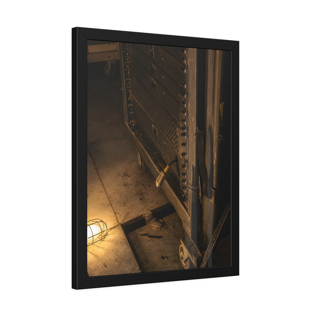 A server rack on a concrete floor beside a caged work light. The Silence at Cutover by Garabaggio, framed fine art print hanging in a room.