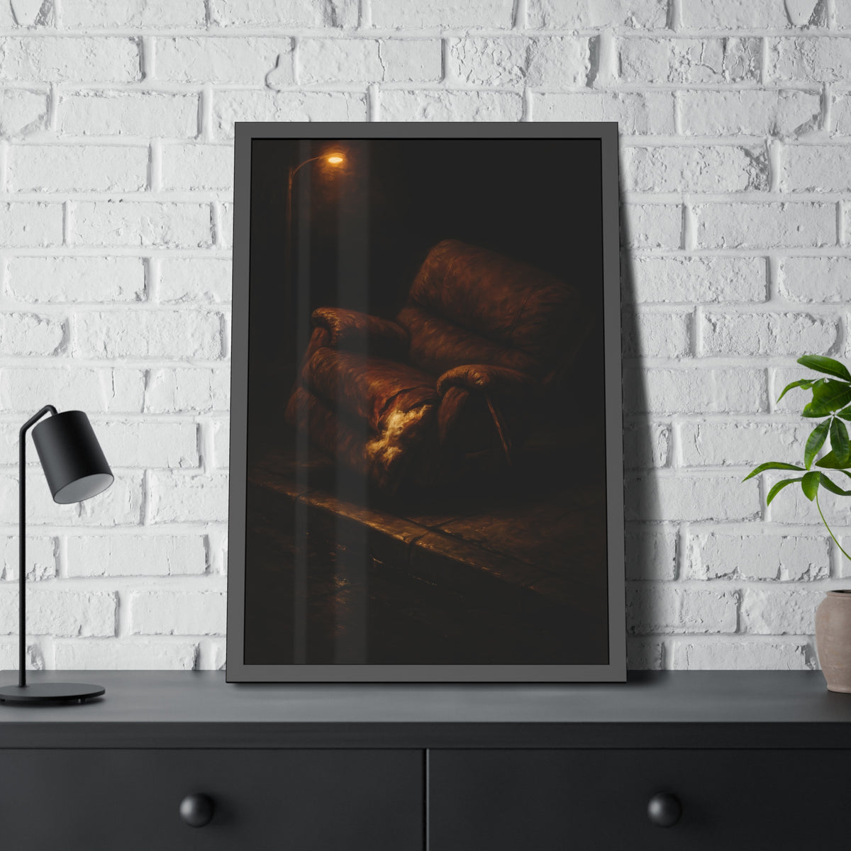 A torn brown recliner tipped on a curb in dim warm light. The Deposition of the Broken Recliner by Garabaggio, framed fine art print hanging in a room.