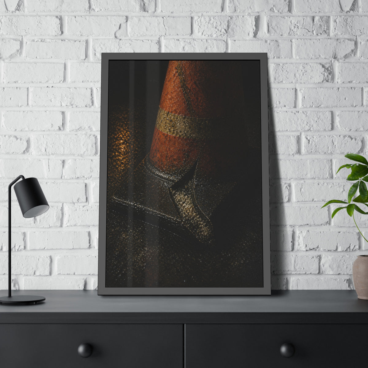 An orange traffic cone with a split base on wet asphalt at night. The Splitting of the Base by Garabaggio, framed fine art print hanging in a room.