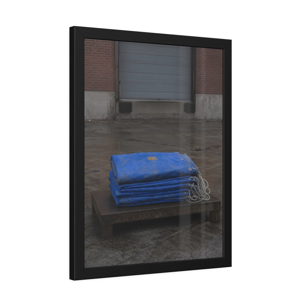 A folded blue tarp stacked on a low wooden platform by a loading dock. The Repaired Fold by Garabaggio, framed fine art print hanging in a room.