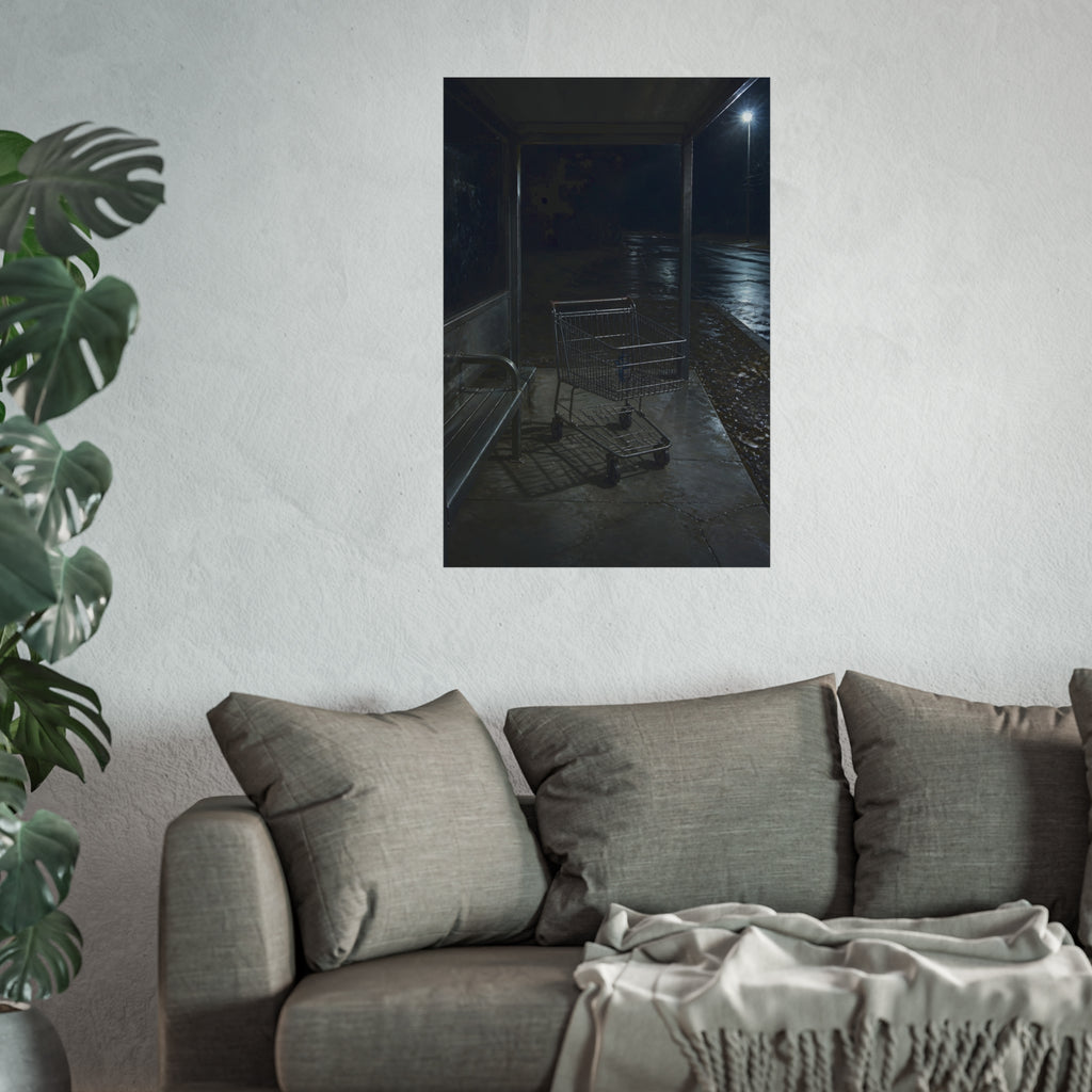 A shopping cart parked inside a bus shelter under a street lamp at night. The Rest at the Bus Shelter by Garabaggio, fine art print hanging in a room.