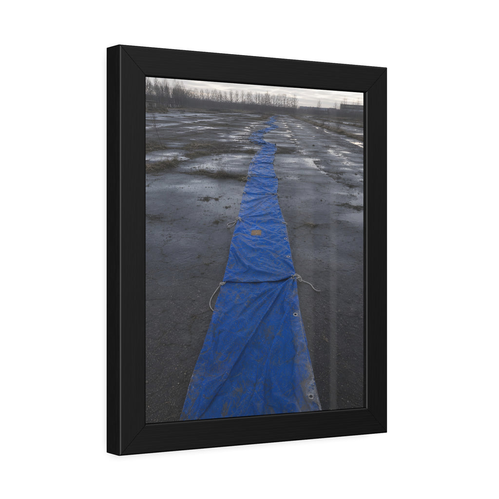 A blue tarp laid in a long strip down a wet cracked lot under grey sky. The Long Ground Procession by Garabaggio, framed fine art print hanging in a room.