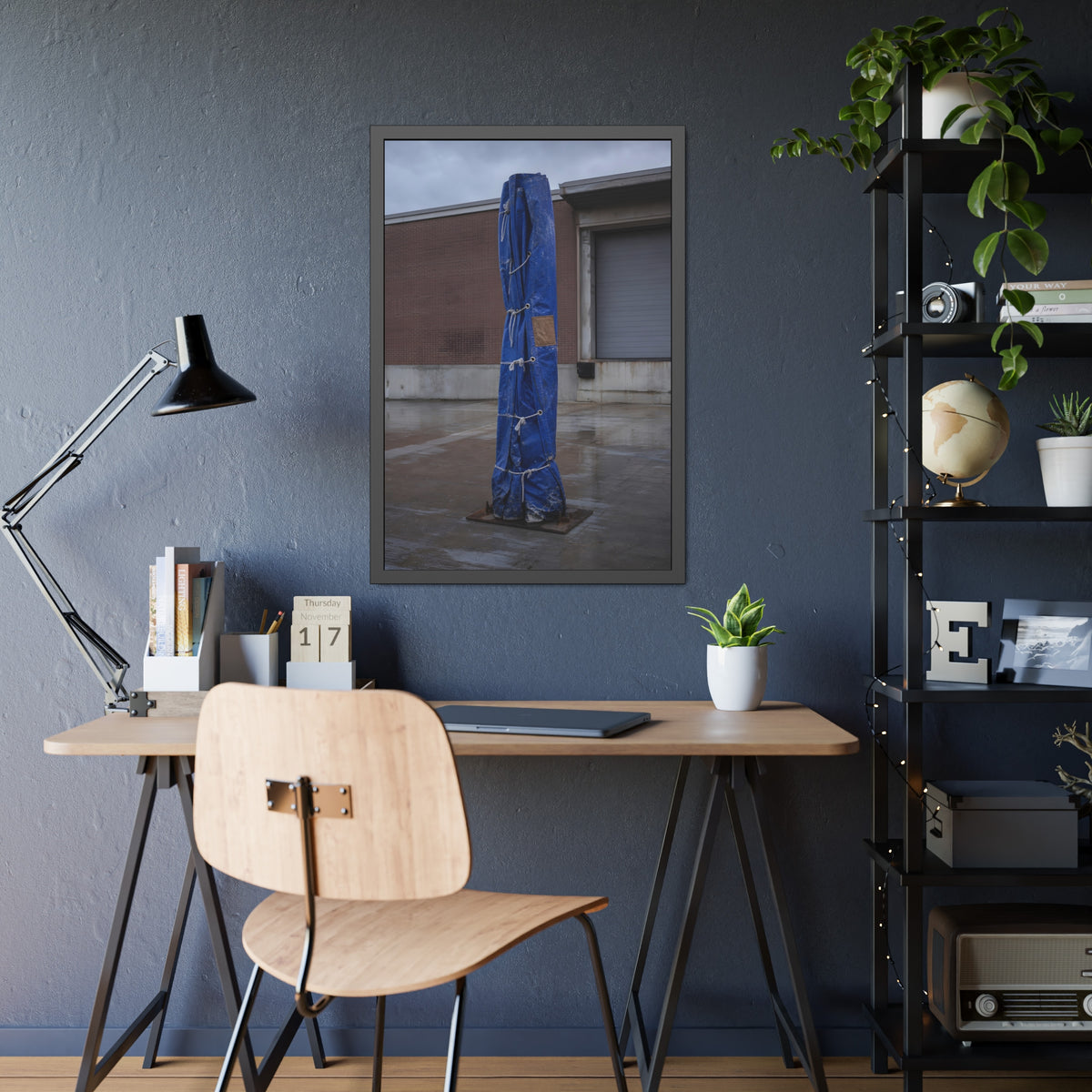 A tall blue tarp bundle roped upright on a wet lot by a loading dock. Folded Standard at the Loading Bay by Garabaggio, framed fine art print hanging in a room.