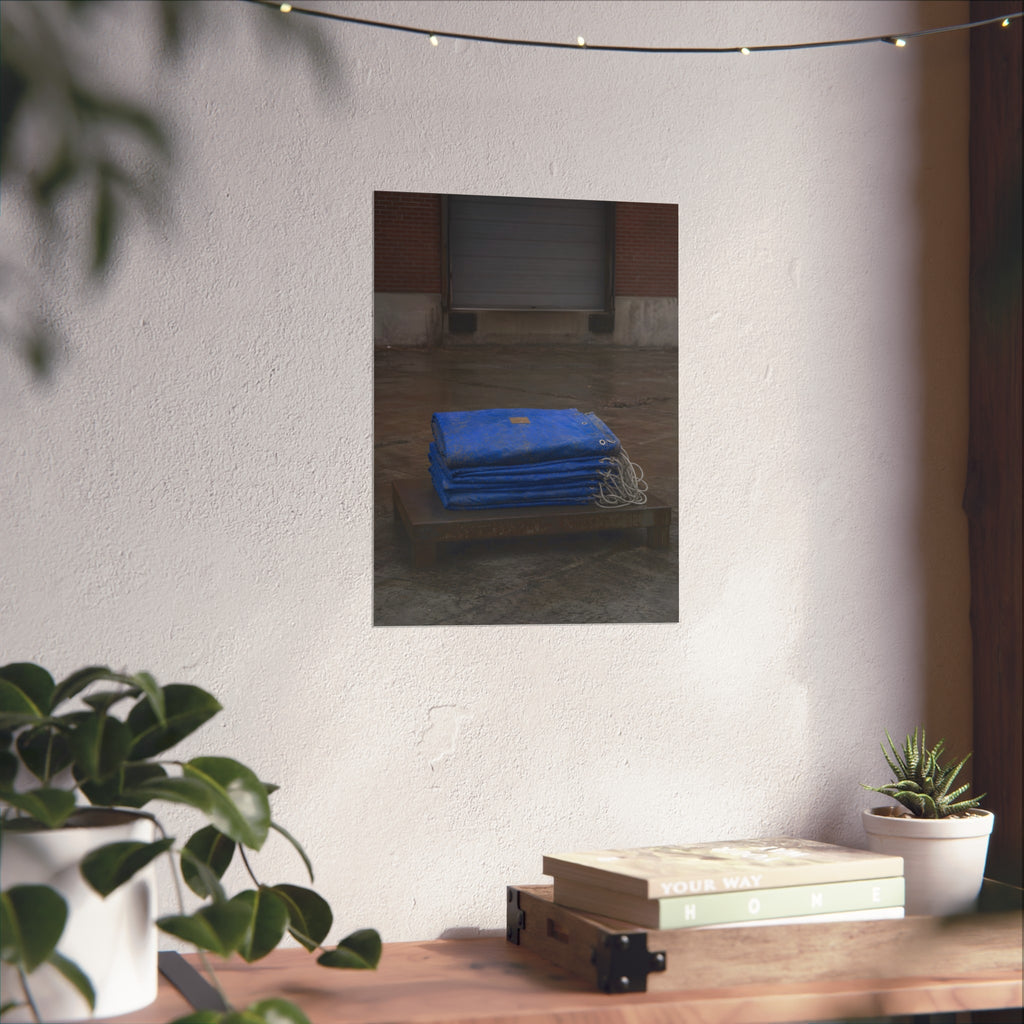 A folded blue tarp stacked on a low wooden platform by a loading dock. The Repaired Fold by Garabaggio, fine art print hanging in a room.