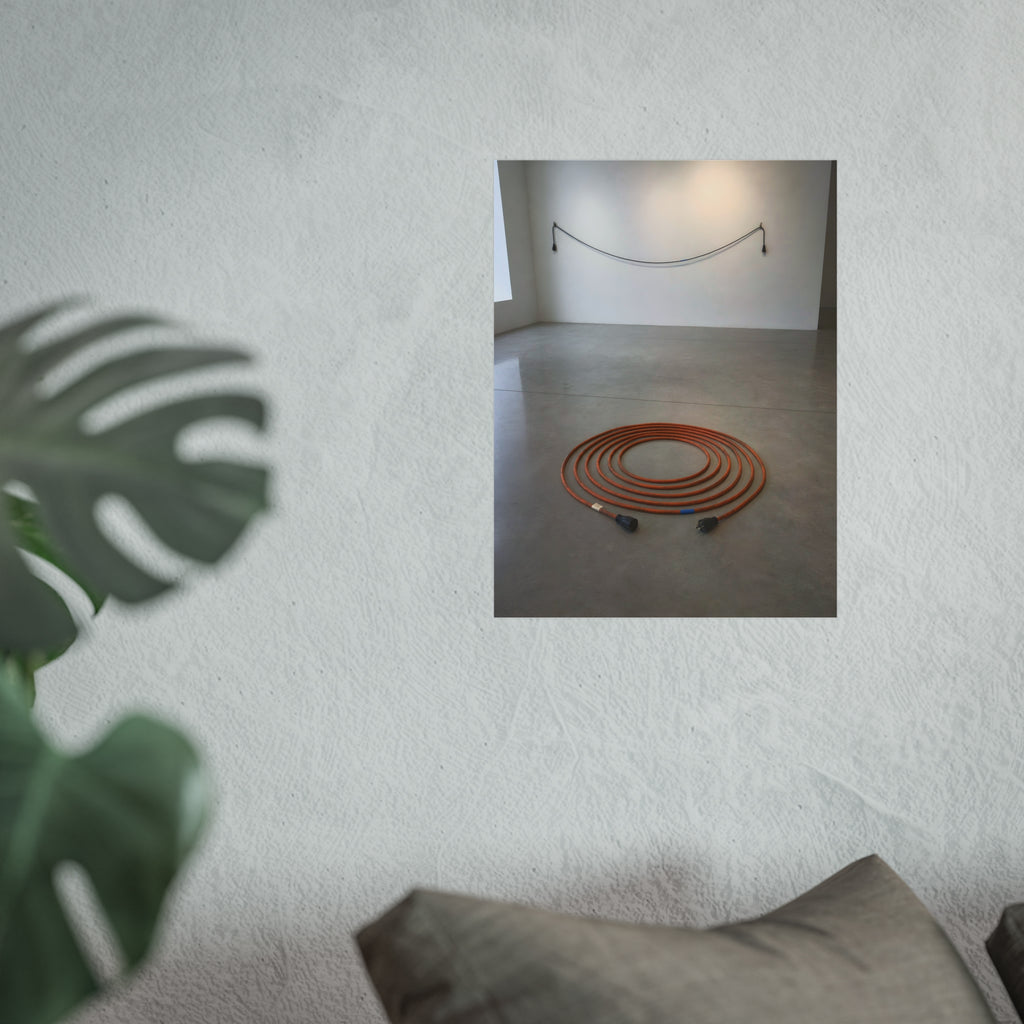An orange extension cord coiled in a spiral on a bare gallery floor. The Floor Coil by Garabaggio, fine art print hanging in a room.