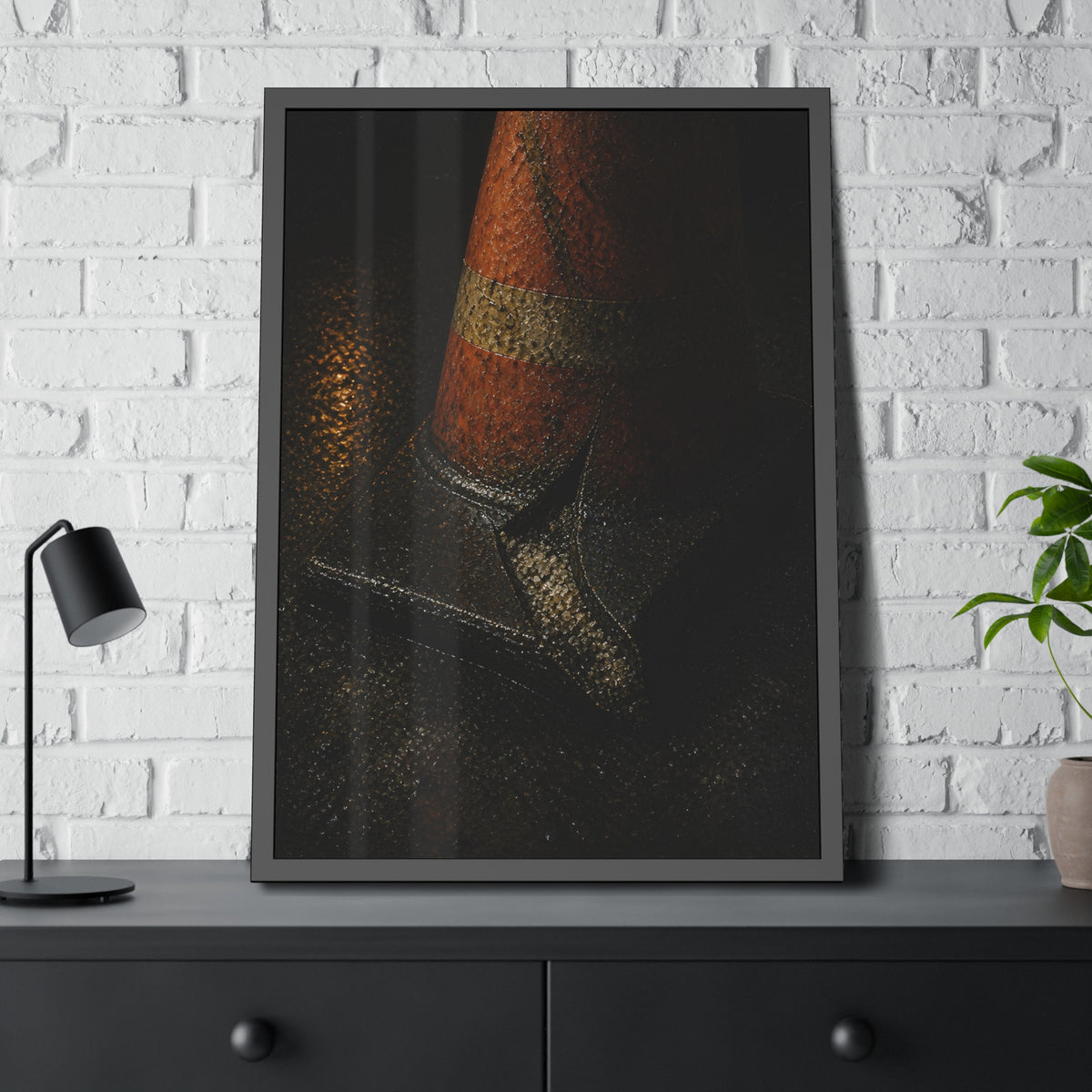 An orange traffic cone with a split base on wet asphalt at night. The Splitting of the Base by Garabaggio, framed fine art print hanging in a room.