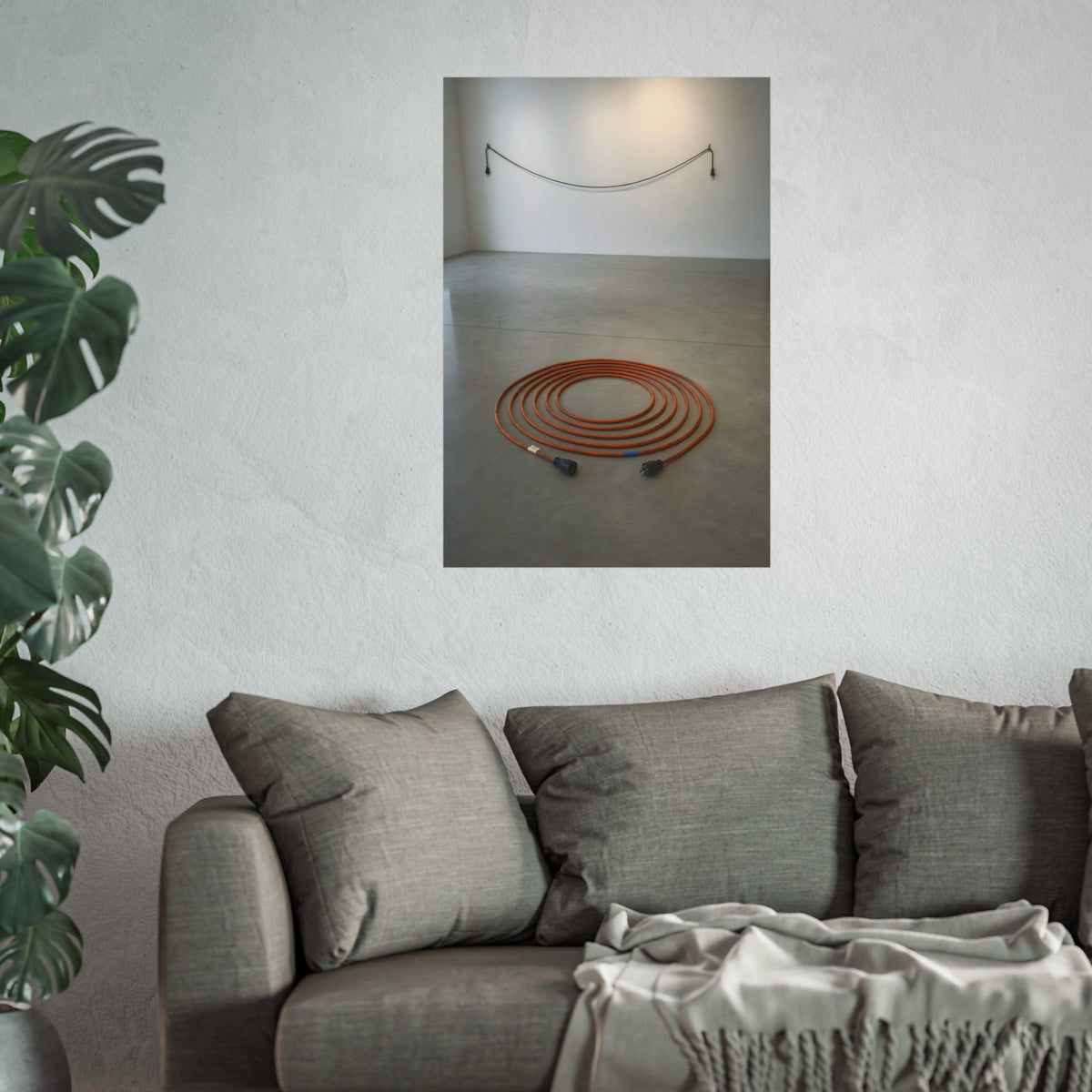 An orange extension cord coiled in a spiral on a bare gallery floor. The Floor Coil by Garabaggio, fine art print hanging in a room.