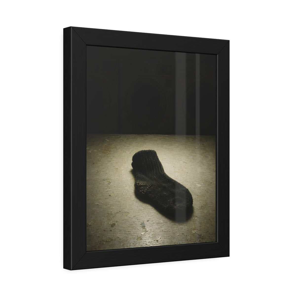 A single dark sock on a laundromat floor before dim washing machines. The Orphaned Sock by Garabaggio, framed fine art print hanging in a room.