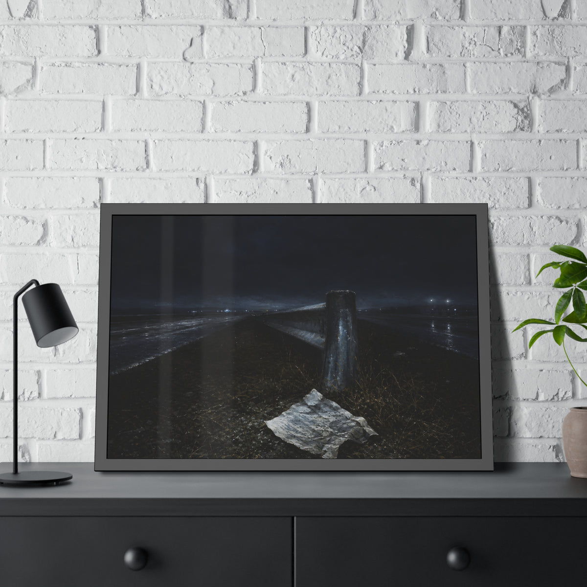A sheet of paper on a grassy highway median beside a concrete post at night. The Resume on the Median by Garabaggio, framed fine art print hanging in a room.