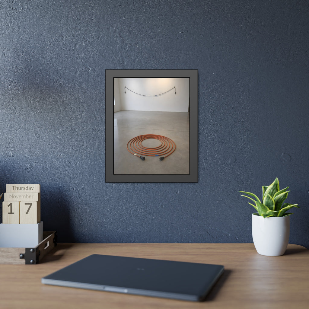 An orange extension cord coiled in a spiral on a bare gallery floor. The Floor Coil by Garabaggio, framed fine art print hanging in a room.