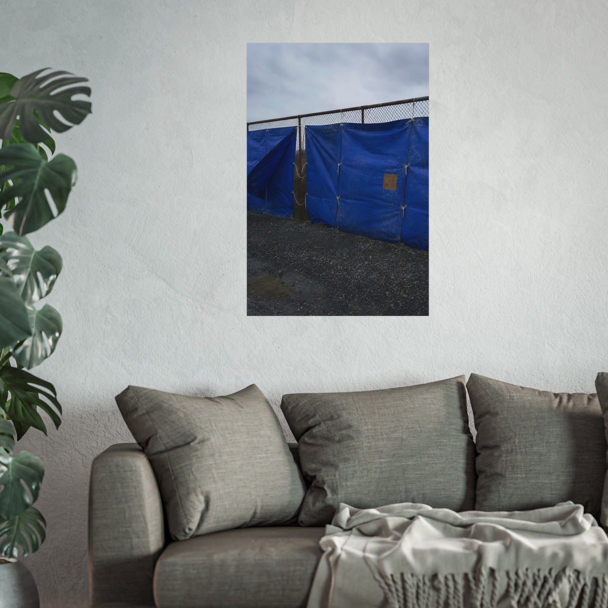 Blue tarps lashed to a chain link fence above gravel under grey sky. Drapery on the Fence by Garabaggio, fine art print hanging in a room.