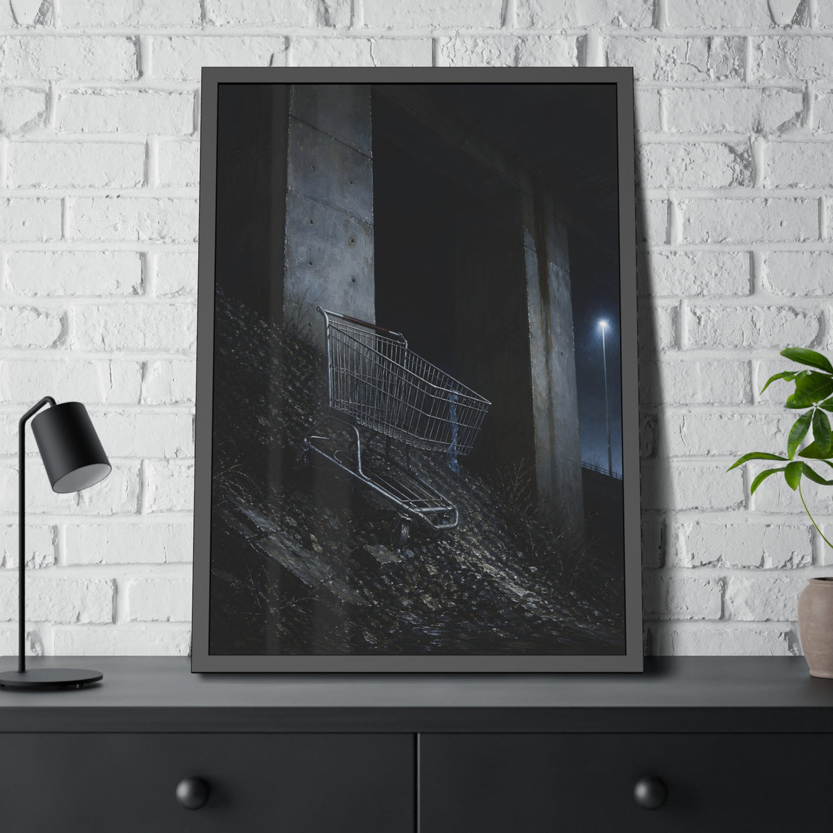 A shopping cart on a rocky slope under an overpass near a streetlamp. The Descent to the Underpass by Garabaggio, framed fine art print hanging in a room.