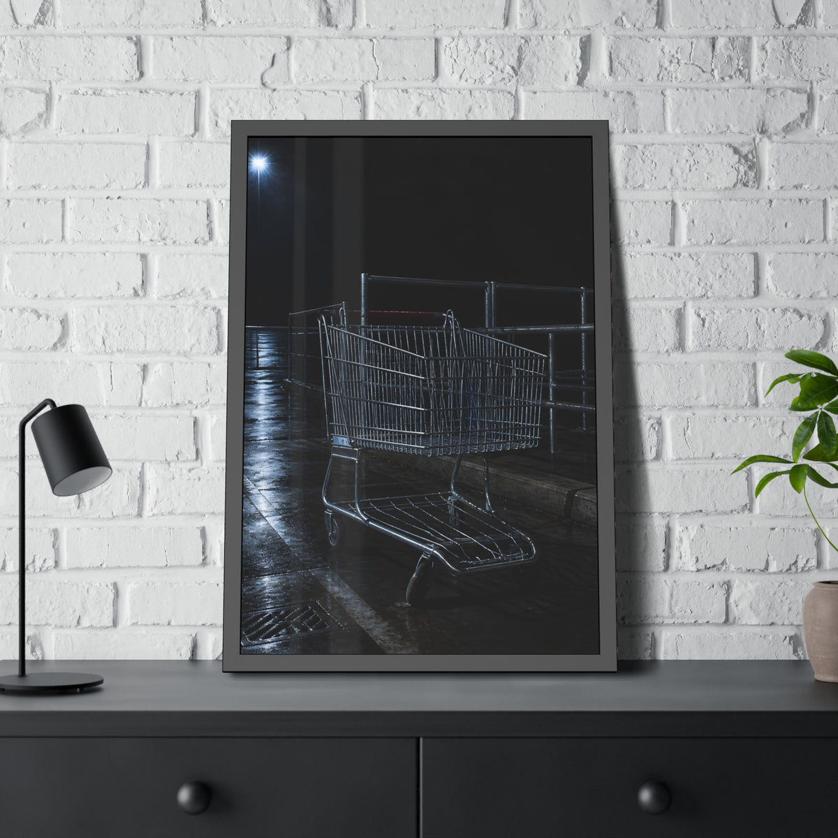 A shopping cart beside its corral on wet asphalt under a lot light. The Cart at the Corral by Garabaggio, framed fine art print hanging in a room.