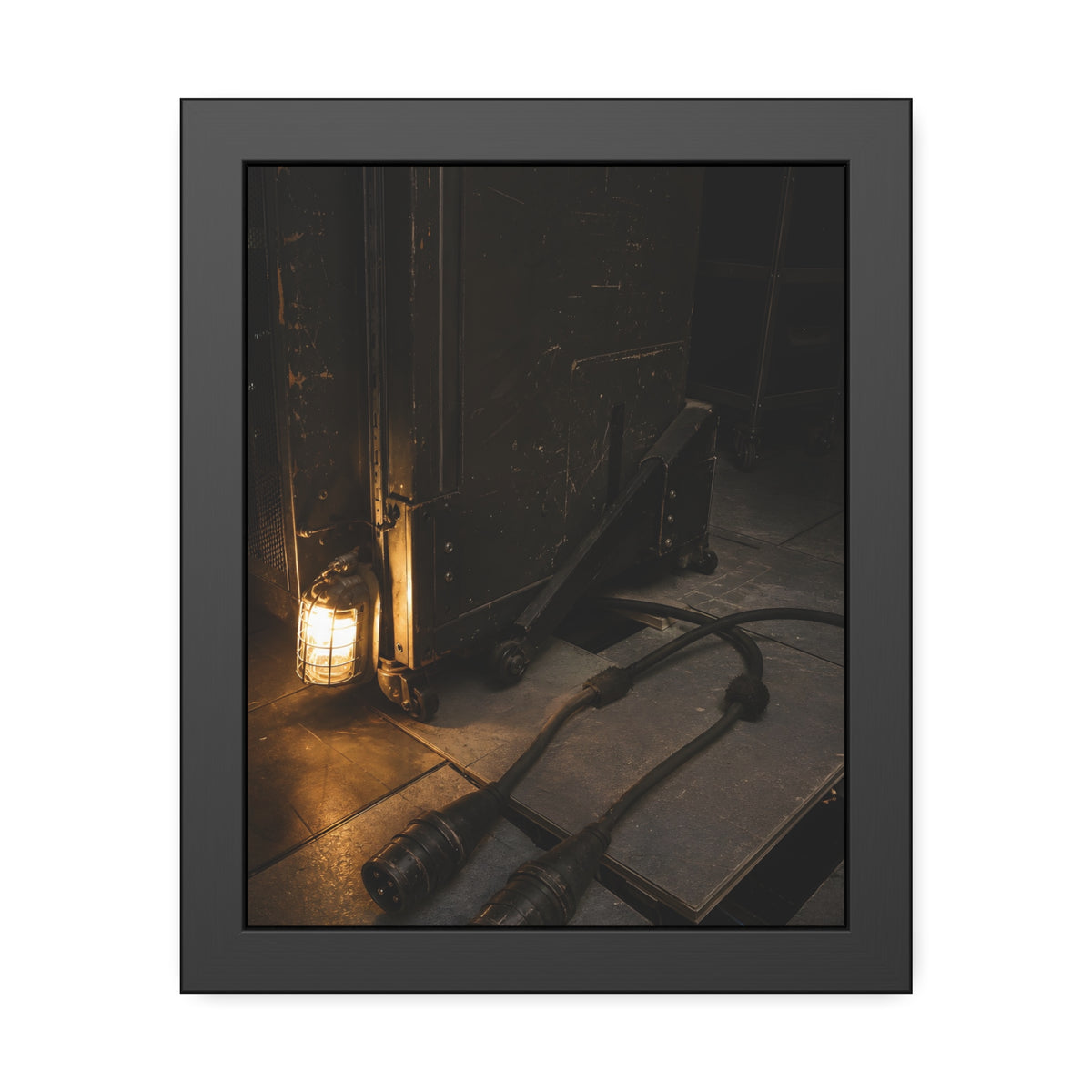 Two thick power cables unplugged on the floor beside a caged work lamp. The Redundant Power by Garabaggio, framed fine art print, 11″ x 14″.