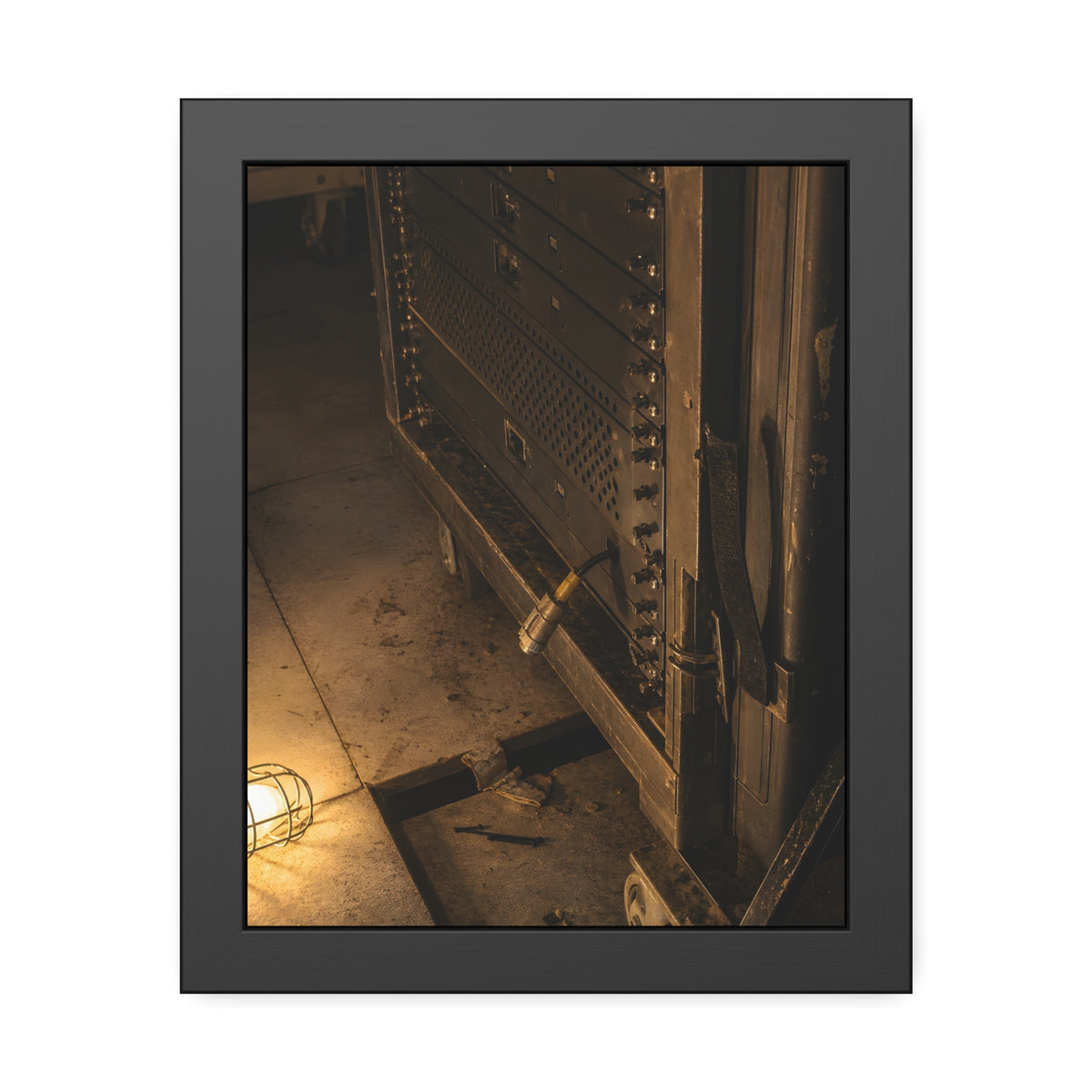 A server rack on a concrete floor beside a caged work light. The Silence at Cutover by Garabaggio, framed fine art print, 11″ x 14″.