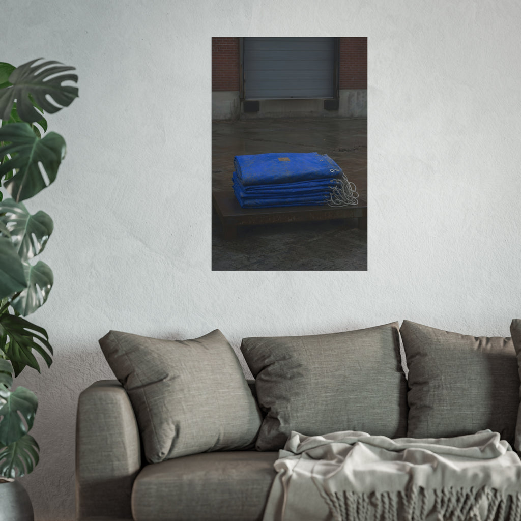 A folded blue tarp stacked on a low wooden platform by a loading dock. The Repaired Fold by Garabaggio, fine art print hanging in a room.