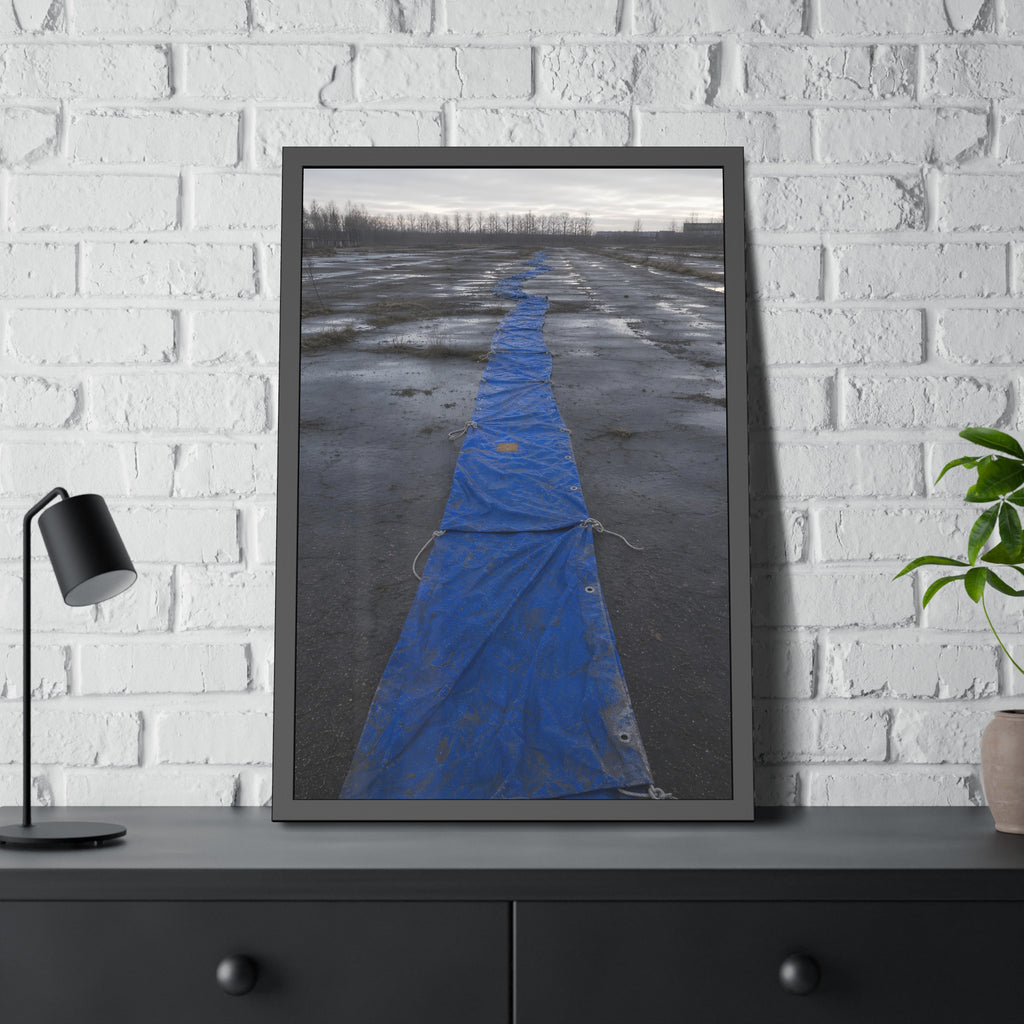 A blue tarp laid in a long strip down a wet cracked lot under grey sky. The Long Ground Procession by Garabaggio, framed fine art print hanging in a room.