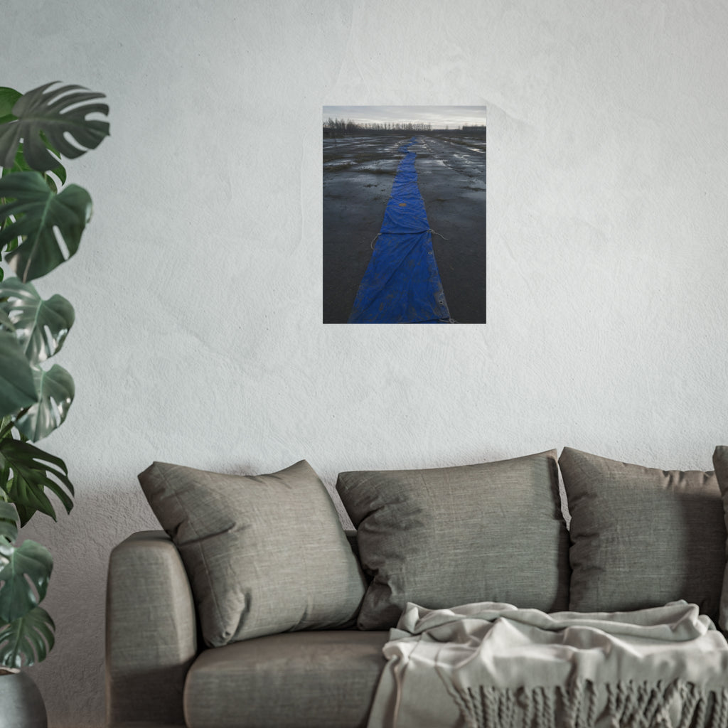 A blue tarp laid in a long strip down a wet cracked lot under grey sky. The Long Ground Procession by Garabaggio, fine art print hanging in a room.