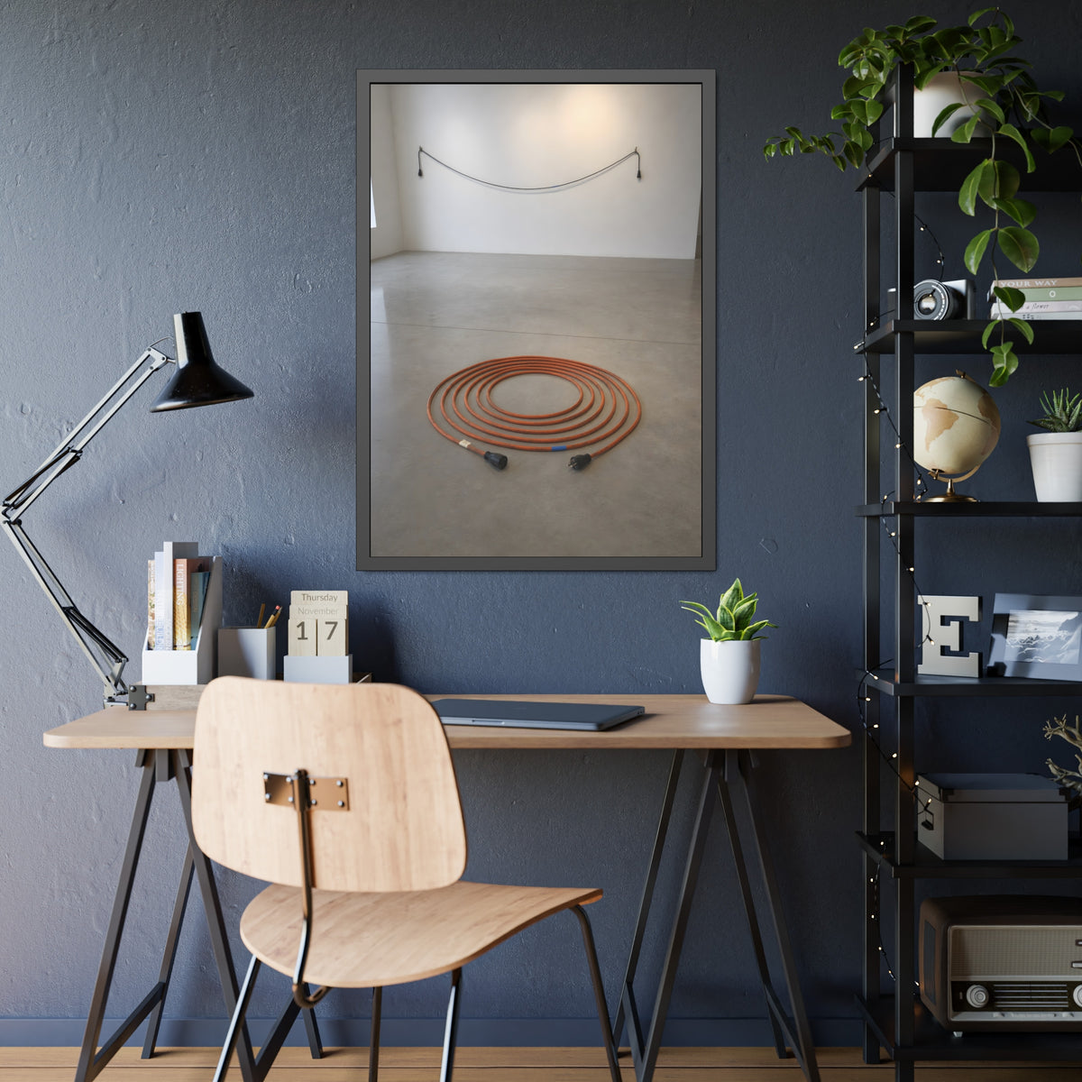 An orange extension cord coiled in a spiral on a bare gallery floor. The Floor Coil by Garabaggio, framed fine art print hanging in a room.