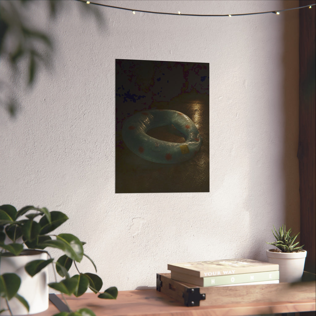 Deflated pool float ring on wet ground, lit from one side in the dark. After the Last Swim by Garabaggio, fine art print hanging in a room.
