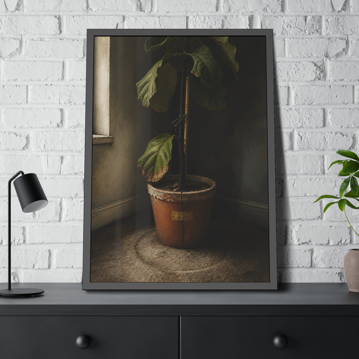 A leafy potted fig staked to a cane in a taped clay pot beside a window. The Corner by the Window by Garabaggio, framed fine art print hanging in a room.
