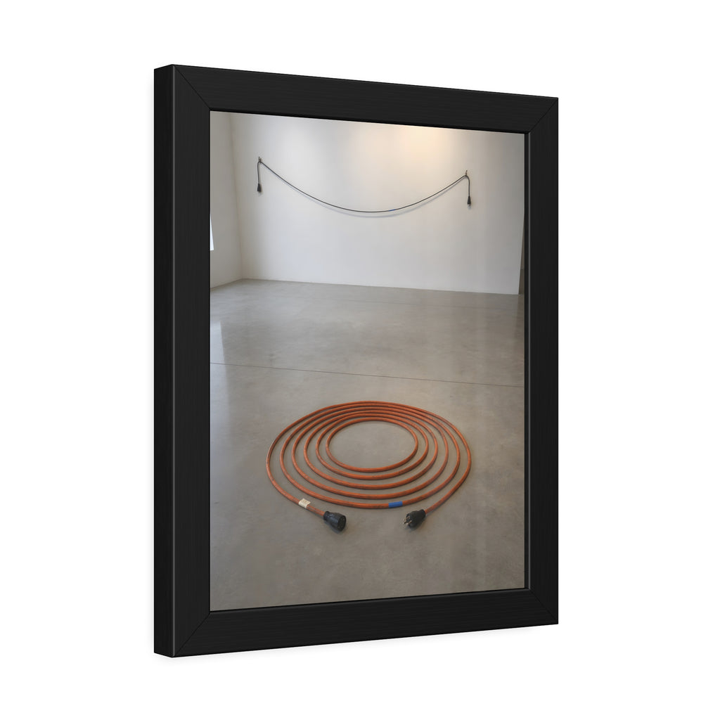 An orange extension cord coiled in a spiral on a bare gallery floor. The Floor Coil by Garabaggio, framed fine art print hanging in a room.