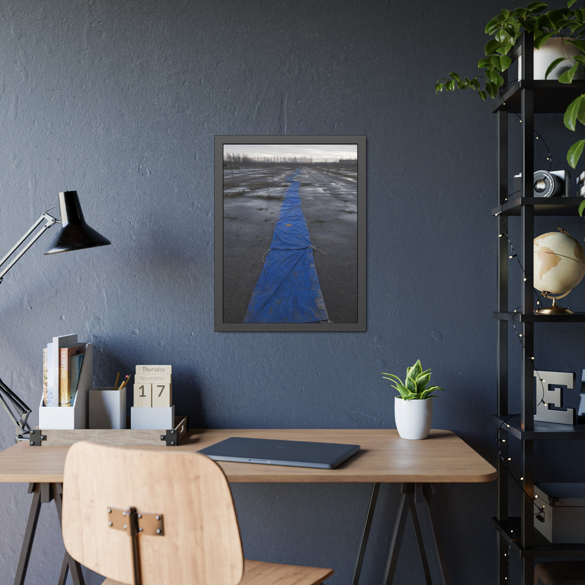 A blue tarp laid in a long strip down a wet cracked lot under grey sky. The Long Ground Procession by Garabaggio, framed fine art print hanging in a room.