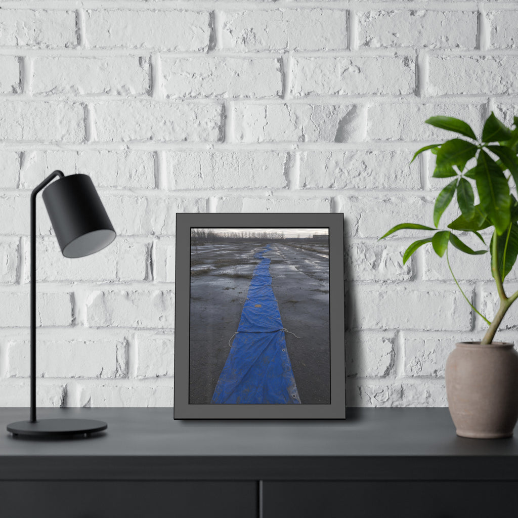 A blue tarp laid in a long strip down a wet cracked lot under grey sky. The Long Ground Procession by Garabaggio, framed fine art print hanging in a room.