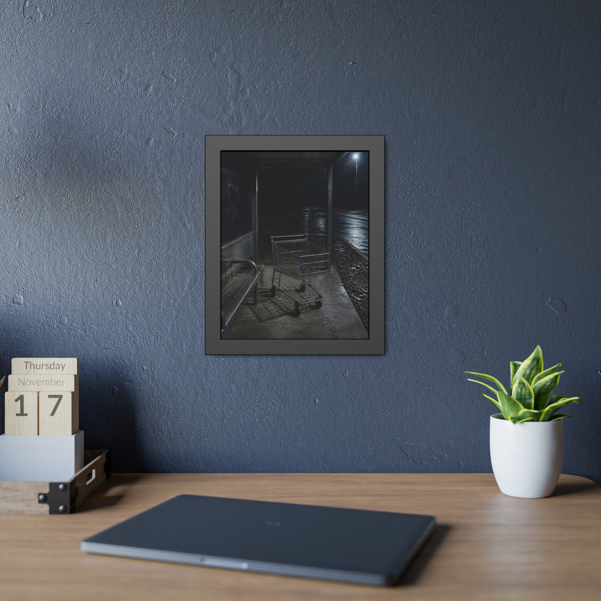 A shopping cart parked inside a bus shelter under a street lamp at night. The Rest at the Bus Shelter by Garabaggio, framed fine art print hanging in a room.