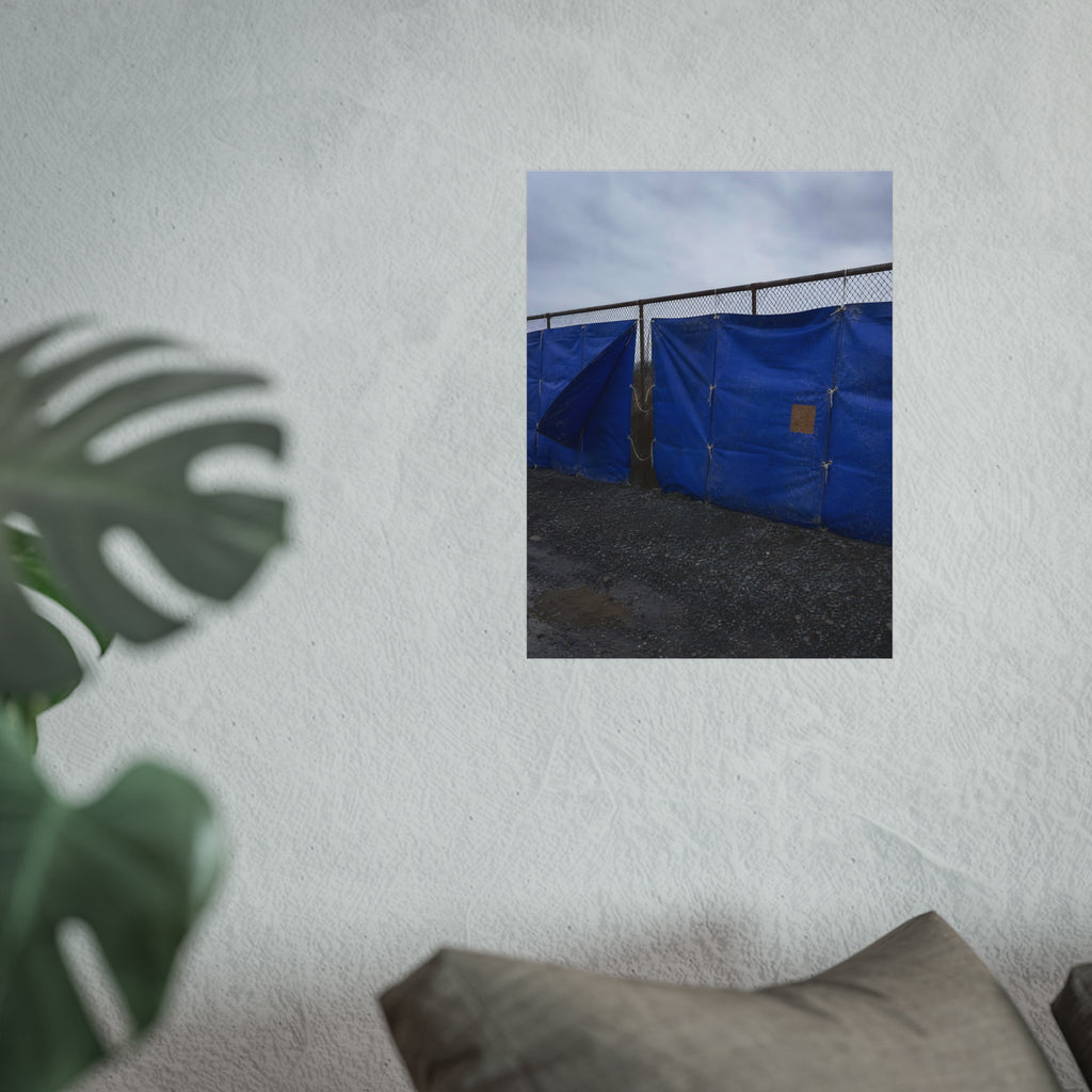 Blue tarps lashed to a chain link fence above gravel under grey sky. Drapery on the Fence by Garabaggio, fine art print hanging in a room.