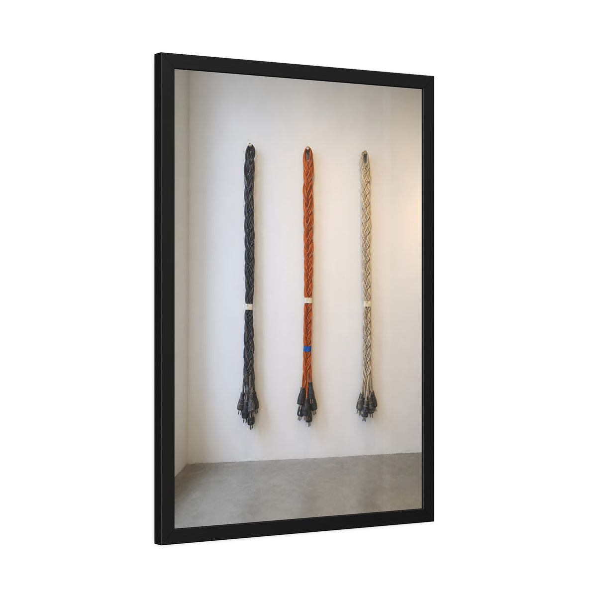 Three braided bundles of extension cords hung on a white gallery wall. The Braided Triptych by Garabaggio, framed fine art print hanging in a room.