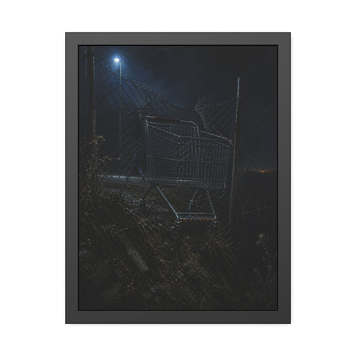 A shopping cart wedged in a chain link fence under a streetlamp. The Abandonment at the Ravine Fence by Garabaggio, framed fine art print, 18″ x 24″.