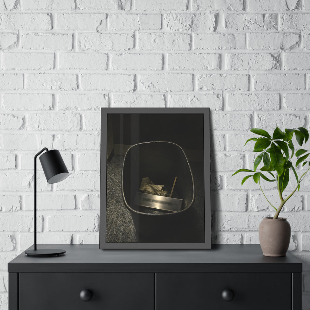 A metal nameplate lying in a black office waste bin on grey carpet. The Nameplate in the Waste Bin by Garabaggio, framed fine art print hanging in a room.