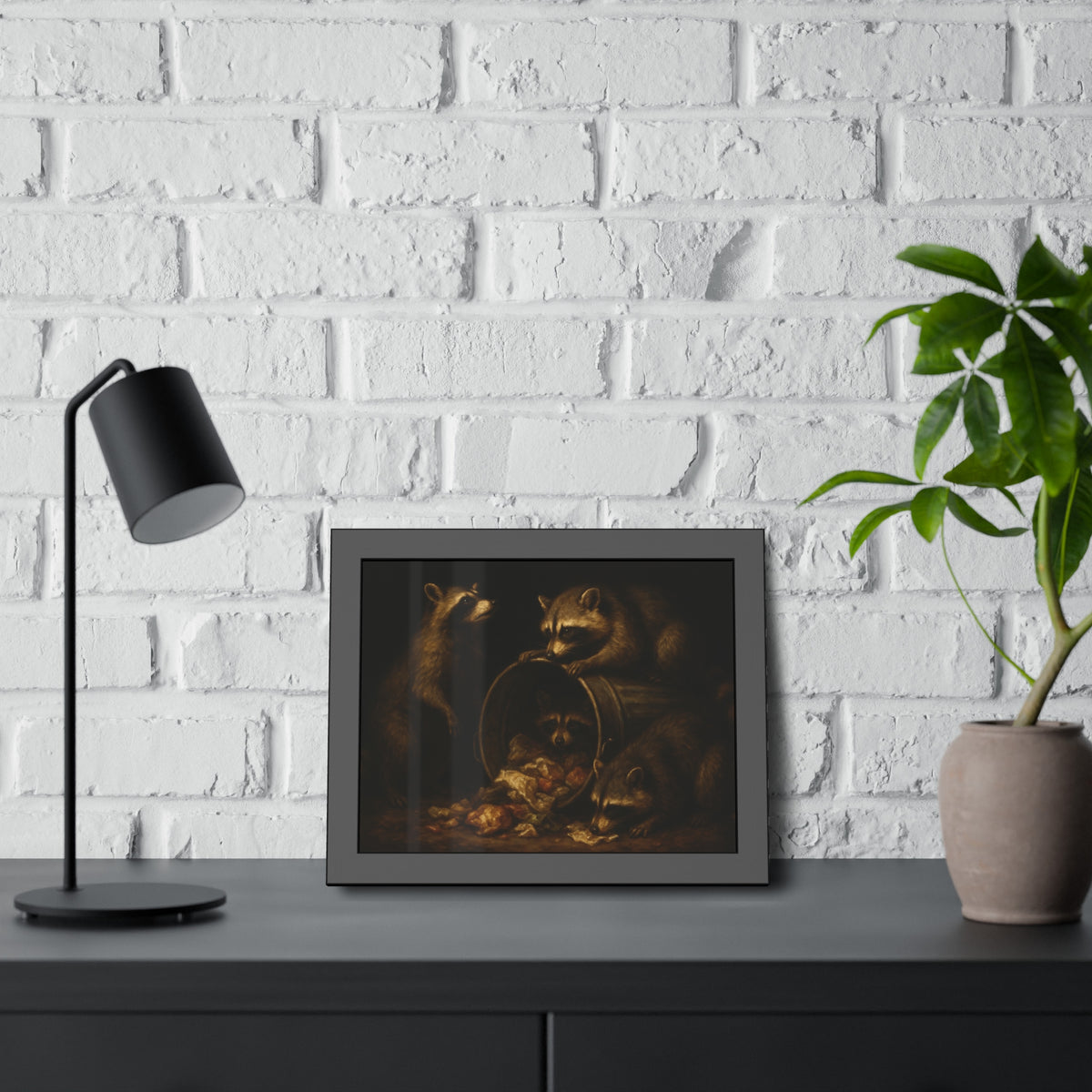 Four raccoons around a tipped metal trash can spilling food scraps. The Crowning with Crumbs by Garabaggio, framed fine art print hanging in a room.