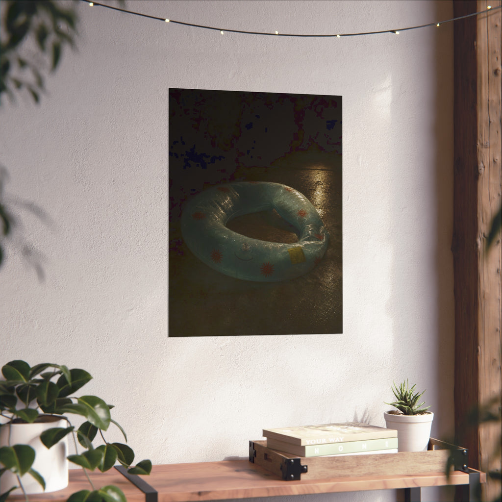 Deflated pool float ring on wet ground, lit from one side in the dark. After the Last Swim by Garabaggio, fine art print hanging in a room.