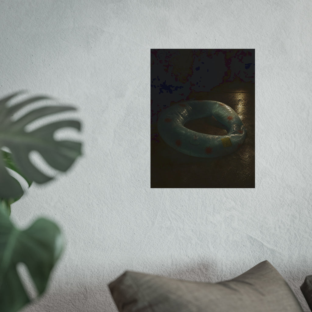 Deflated pool float ring on wet ground, lit from one side in the dark. After the Last Swim by Garabaggio, fine art print hanging in a room.