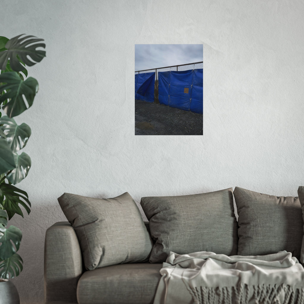 Blue tarps lashed to a chain link fence above gravel under grey sky. Drapery on the Fence by Garabaggio, fine art print hanging in a room.