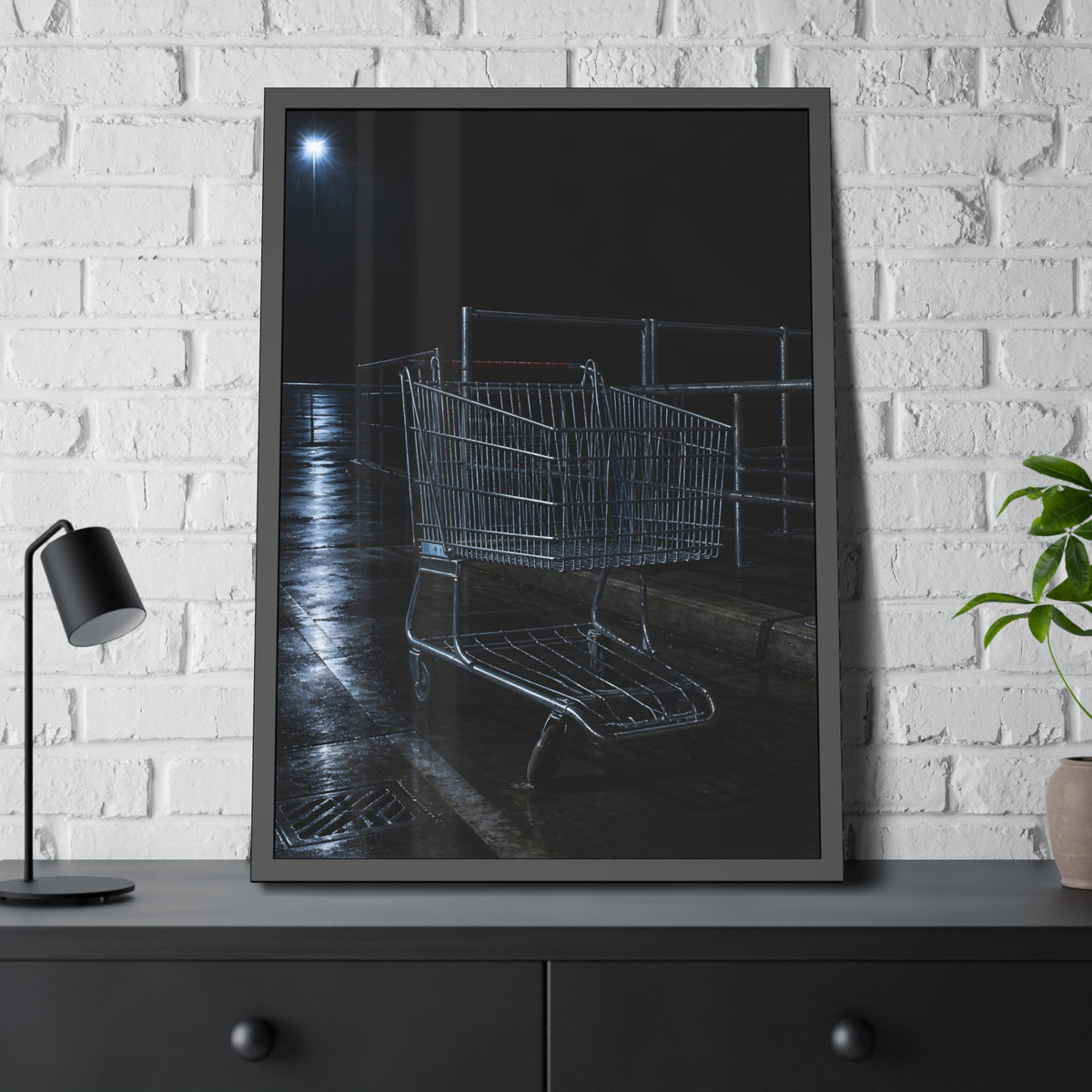 A shopping cart beside its corral on wet asphalt under a lot light. The Cart at the Corral by Garabaggio, framed fine art print hanging in a room.