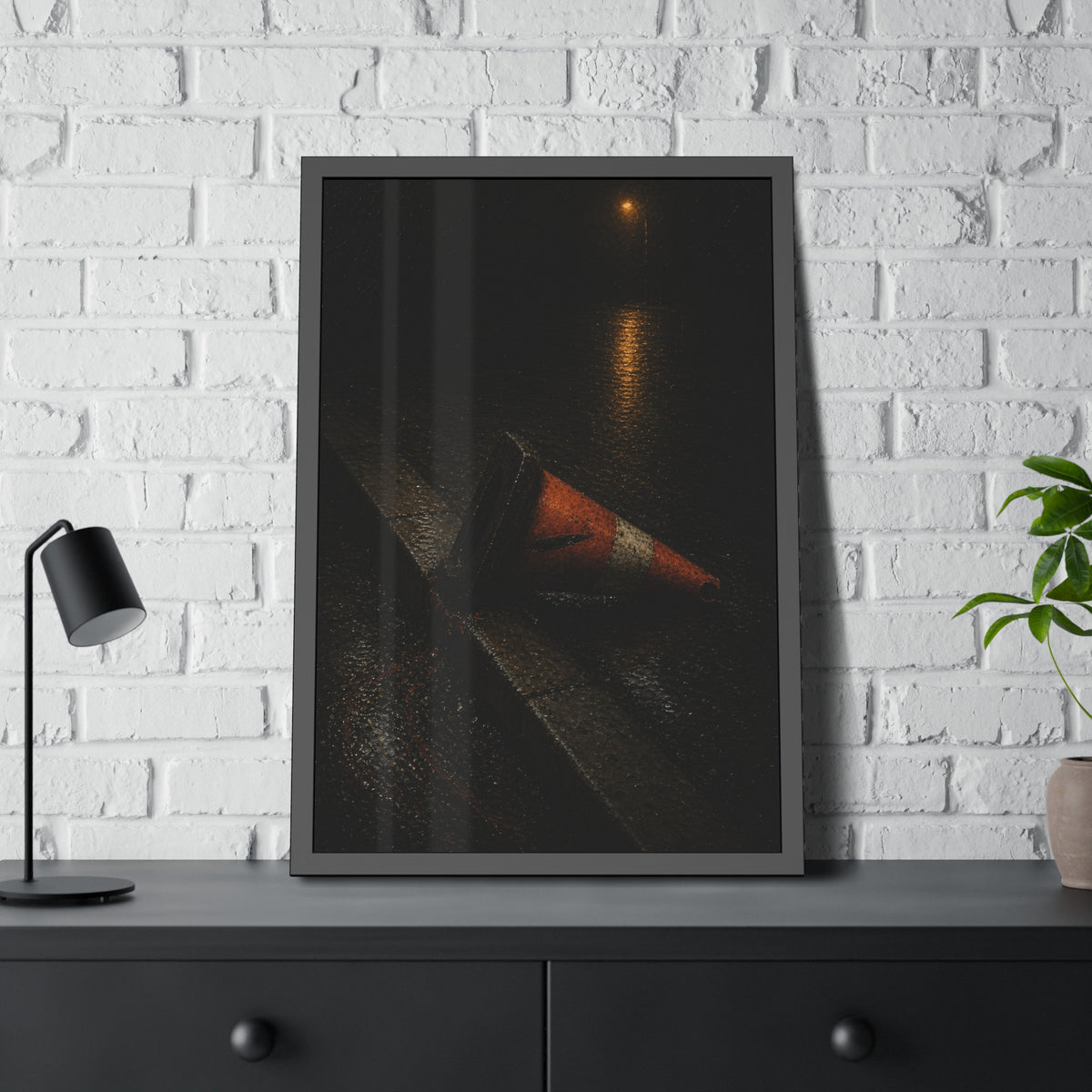 An orange traffic cone toppled on a wet curb under a distant streetlamp. The Dragging Through Rain by Garabaggio, framed fine art print hanging in a room.