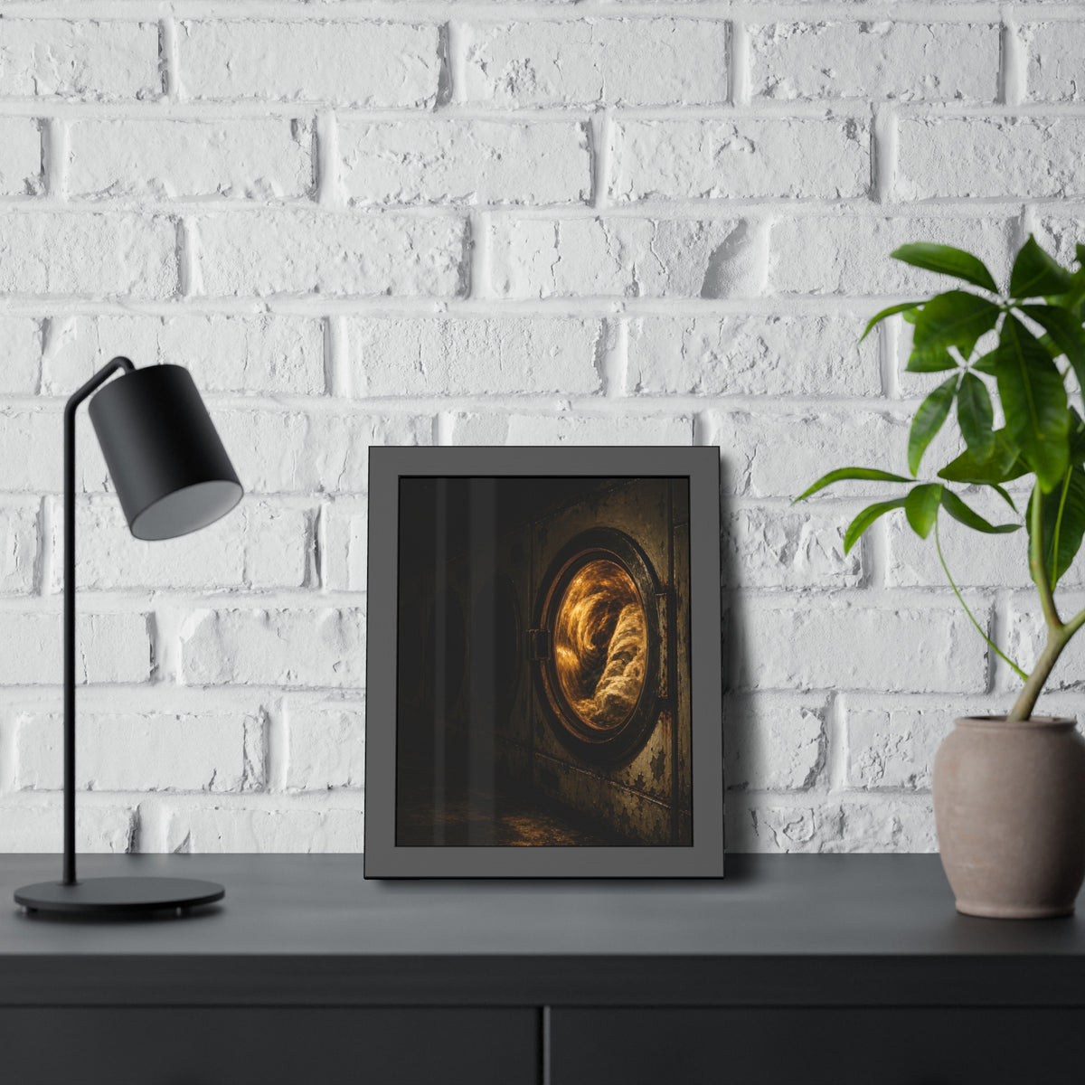 A row of dryers with one drum lit and tumbling in a dark laundromat. The Last Dryer Turning by Garabaggio, framed fine art print hanging in a room.